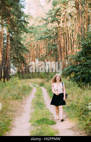 Junge hübsche Plus Size kaukasischen glücklich lächelnde Mädchen Frau im weißen T-Shirt und schwarzen kurzen Rock zu Fuß unterwegs im Sommer Kiefernwald in voller Länge Stockfoto