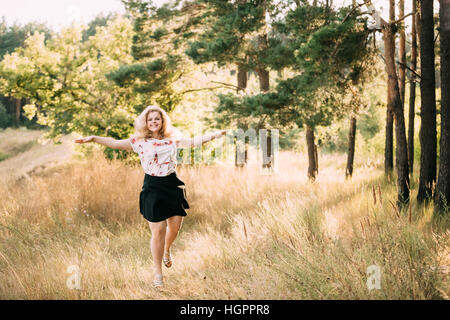 Einzelne junge hübsche Plus Size kaukasischen glücklich lächelnde lachende Mädchen Frau im weißen T-Shirt, im Sommer grün Wald tanzen. Spaß im freien Sommer N Stockfoto