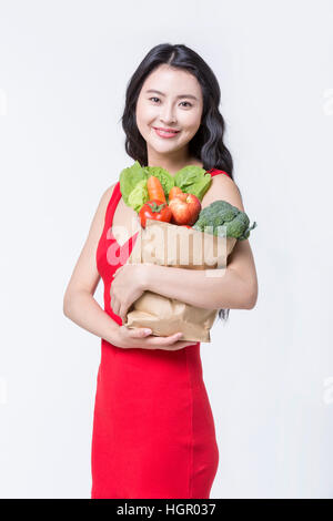 Junge lächelnde Frau in rotem Kleid hält einen Beutel mit Gemüse Stockfoto