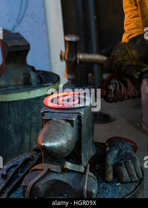 Der Schmied schmieden manuell das geschmolzene Metall auf dem Amboss in Schmiede mit Funken Feuerwerk Stockfoto