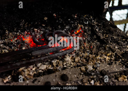 Der Schmied schmieden manuell das geschmolzene Metall auf dem Amboss in Schmiede mit Funken Feuerwerk Stockfoto