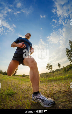 Junger Mann Joggen im Freien. Beine eines Mannes mit einem niedrigen Winkel. Vor dem Hintergrund des blauen Himmels mit Flecken von Sonnenlicht. Stockfoto