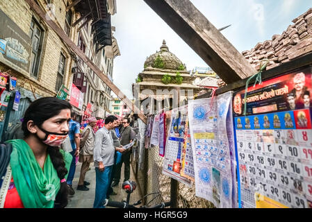 Eine Frau trägt eine Staubmaske, während sie auf Kalender achtet, die in einem Straßenladen in Kathmandu, Nepal, verkauft werden. Stockfoto
