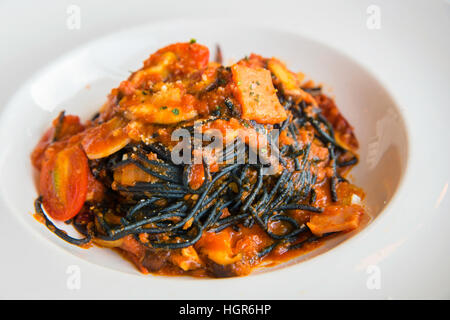 Schwarze Spaghetti-Sauce, Chili, Meeresfrüchte mit rohen Tomaten in weiße Scheibe. Stockfoto