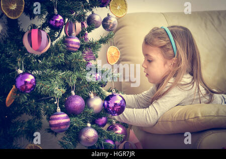 Kleines Mädchen ist dekorieren Weihnachtsbaum mit hausgemachten Ornamente in Retro-Filter-Effekt oder Instagram-filter Stockfoto