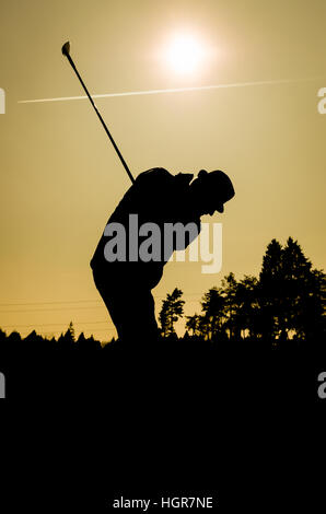 Silhouette der alten Mann Golf zu spielen. Senioren ist trägt einen Hut und schwingen den Club mit Sonne und Flugzeug-Kondensstreifen im Hintergrund. Auch eine si Stockfoto