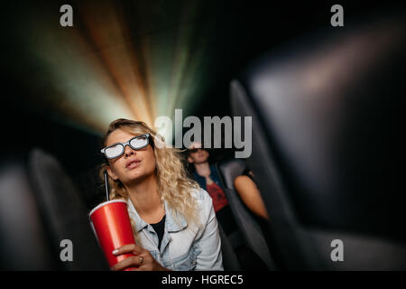 Schöne junge Frau mit Kaltgetränk und 3D-Brille Film im Theater. Stockfoto