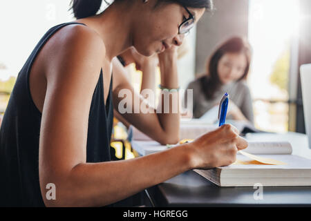 Schuss von jungen Studentinnen Schreiben von Notizen mit Klassenkameraden im Hintergrund lesen hautnah. Studenten in der Uni-Bibliothek. Stockfoto