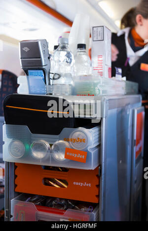 Ein Trolley Wagen während einem Easyjet Flug. Flugbegleiter / Luft Stewardess serviert Getränke / snacks Passagiere & wird die Zahlung von Geld Stockfoto