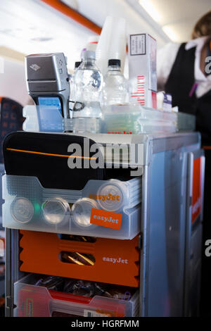 Ein Trolley Wagen während einem Easyjet Flug. Flugbegleiter / Luft Stewardess serviert Getränke / snacks Passagiere & wird die Zahlung von Geld Stockfoto