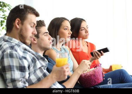 Seitenansicht der gelangweilte Gruppe von vier Freunden, die gerade eines schlechte tv-Programms sitzen auf einem Sofa im Wohnzimmer einer Wohnung Stockfoto