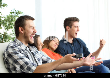 Aufgeregt Männer vor dem Fernseher und gelangweilte Freundinnen sitzen auf einer Couch im Wohnzimmer zu Hause Stockfoto