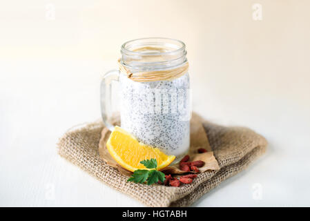 Chia Samen Pudding in einem Glas auf weißem Hintergrund aus Holz, verziert mit Orange und Goji Beeren Stockfoto