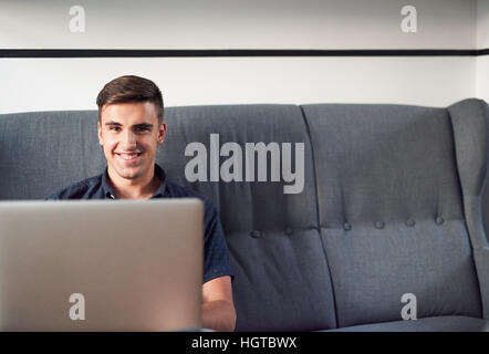 Lächelnder junger Mann mit einem Laptop zu Hause Stockfoto