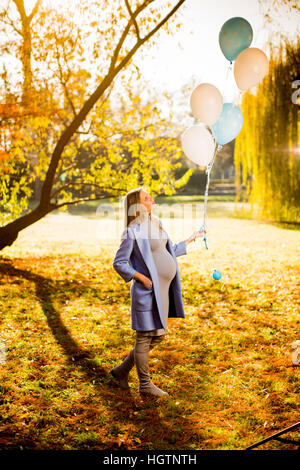 Wiew bei schwangeren Frauen mit bunten Luftballons im herbstlichen Wald Stockfoto