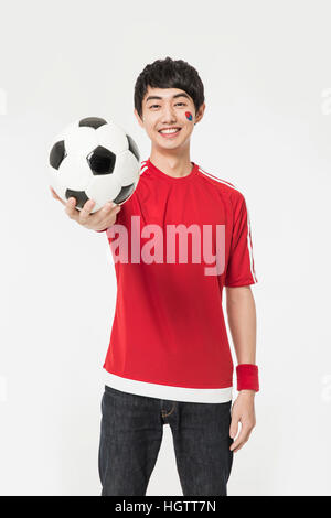 Lächelnde koreanischen Cheerleader Jüngling hält einen Fußball Stockfoto