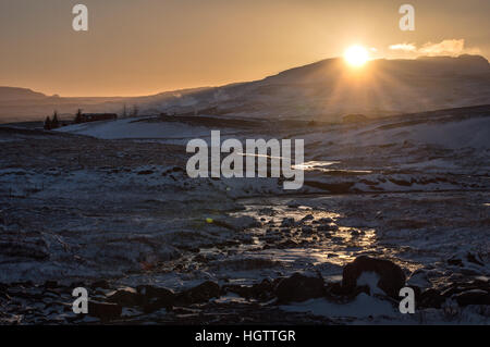 Sonnenuntergang über eine verschneite Landschaft und Bachlauf im Thingvellir National Park in Island. Stockfoto