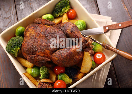 Ganze gegrillte Hühnchen mit Gemüse in Schüssel auf hölzernen Hintergrund Stockfoto