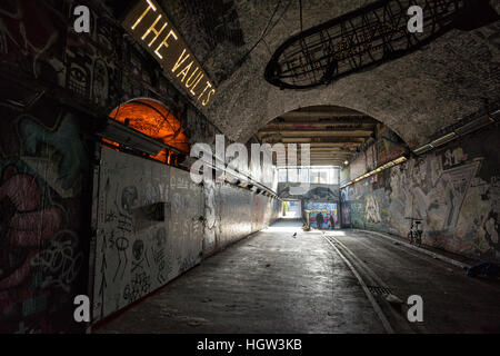 Graffiti-bedeckter Backsteintunnel in der Leake Street, London, mit beleuchtetem „The Vaults“-Schild und Tageslicht, das durch das Ende des Stadtstadts fließt Stockfoto