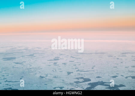 Luftbild aus großer Höhe Flug Flugzeug auf schneebedeckten Boden im Winter bei Sonnenuntergang Sonnenaufgang. Wälder und Felder. Klaren sonnigen Dawn Sky mit Co Stockfoto