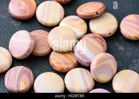 Sammlung von bunten Münze geprägt Hickoryite Perlen auf schwarzen Gussplatte. Hickoryite ist vielfältige Rhyolith gebändert. Stockfoto