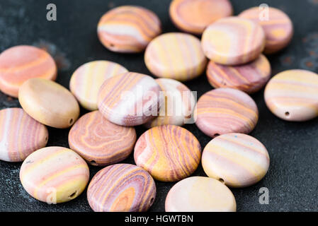 Sammlung von bunten Münze geprägt Hickoryite Perlen auf schwarzen Gussplatte. Hickoryite ist vielfältige Rhyolith gebändert. Stockfoto