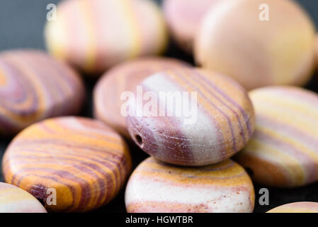 Sammlung von bunten Münze geprägt Hickoryite Perlen auf schwarzen Gussplatte. Hickoryite ist vielfältige Rhyolith gebändert. Stockfoto