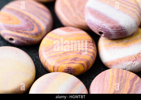 Sammlung von bunten Münze geprägt Hickoryite Perlen auf schwarzen Gussplatte. Hickoryite ist vielfältige Rhyolith gebändert. Stockfoto