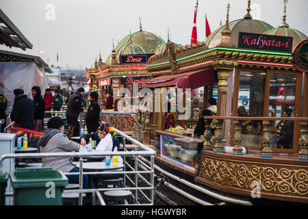 Menschen essen Balik Ekmek ("Fisch im Brot"), gekocht und serviert von farbigen und geschmückten Booten in Istanbul. Stockfoto