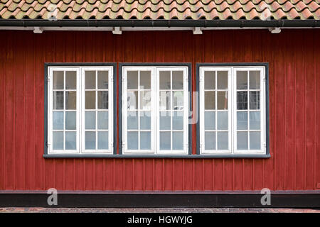 Drei weiß lackiert Flügelfenster mit teilweise gefrostet, Verglasung, in einem rot lackierten Holzbohle Fassade Stockfoto