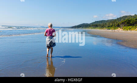 Frau zu Fuß am Strand am Kalaloch Beach, Olympic Nationalpark, Washington State, USA.  Ebbe, blauer Himmel, leere Strände. Stockfoto