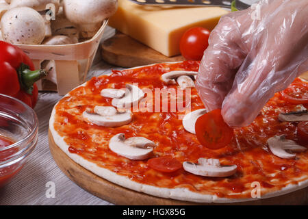 Hand im Handschuh-Chef setzt auf eine Pizza base Cherry-Tomaten. Closeup. Horizontale Stockfoto