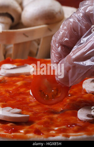 Hand im Handschuh-Chef setzt auf eine Pizza base Cherry-Tomaten. Makro. vertikale Stockfoto