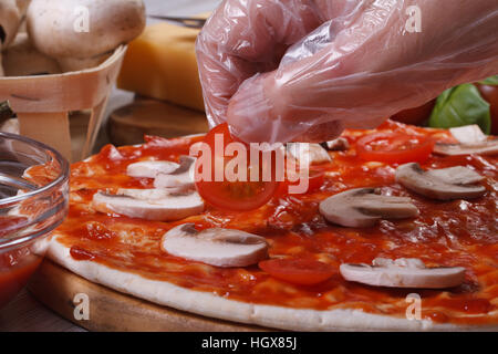 Hand im Handschuh-Chef setzt auf eine Pizza base Cherry-Tomaten. Makro. horizontale Stockfoto