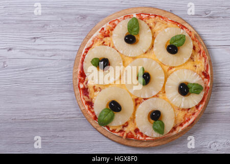 Pizza mit Ananasringe, Oliven und Basilikum auf dem Tisch. Ansicht von oben Stockfoto