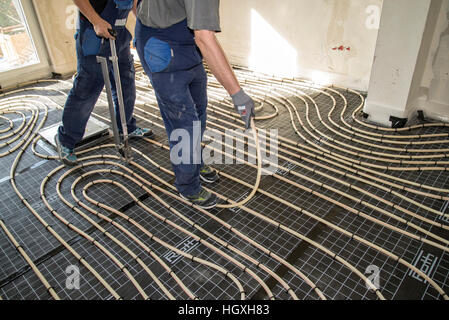 Handwerker bei der Verlegung von Rohrleitungen der Fußbodenheizung Stockfoto