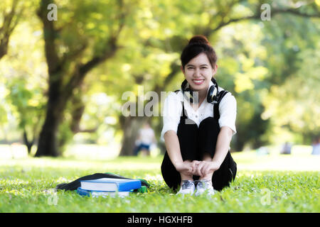 Asiatische Studentin Mädchen draußen im Park anhören von Musik über Kopfhörer während des Studiums Stockfoto