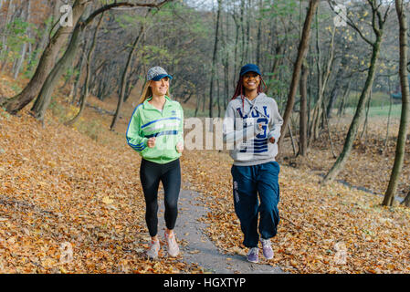 Zwei sportliche Frauen im Herbst Park Joggen. Blond und afrikanische Mädchen. Gelbe Blätter. Frau, Lächeln Stockfoto