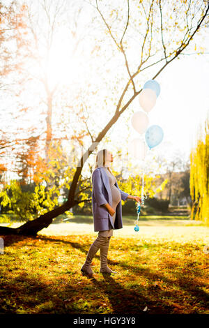 Junge schwangere Frau geht im Herbst Park mit Luftballons in der hand Stockfoto
