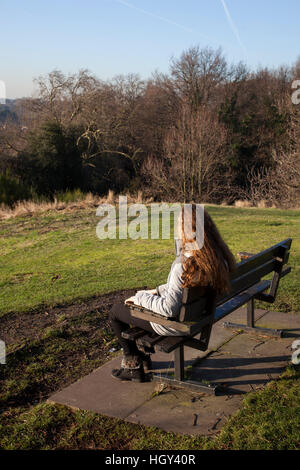 Junge Frau mit langen Haaren zurück zu Kamera, sitzen auf einer Parkbank, Blick in die Ferne. Stockfoto