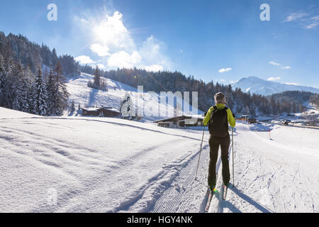 Frau macht Langlaufen auf präparierten Trail im tief verschneiten Winterlandschaft mit sonnigem Wetter und wunderschönen Bergen im Hintergrund Stockfoto