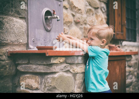 Kleiner Junge Händewaschen unter dem Wasserhahn im Garten