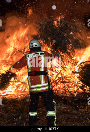 Gundelfingen, Deutschland. 14. Januar 2017. Ein Feuerwehrmann wirft einen Weihnachtsbaum in ein riesiges Feuer in Gundelfingen, Deutschland, 14. Januar 2017. Die Gemeinde sammelt alle Weihnachtsbaum um sie außerhalb der Stadt in einem Feuer zu verbrennen, die mehrere hundert Bewohner für sammeln. Foto: Patrick Seeger/Dpa/Alamy Live News Stockfoto