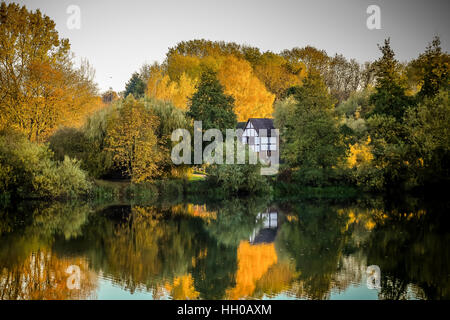 Eine herbstliche oder Herbst, Szene mit Bäumen reflektiert in einem See. Gibt es einen schwarzen und weißen Fachwerkhaus, versteckt in den Wäldern Stockfoto