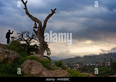 Lalibela, Amhara Region, Äthiopien. Ein Mann Fotografieren aus einem Hügel Hügel gekrönt von einem alten Baum hängt eine große Glocke der Stadt Lalibela. Lalibela Stockfoto