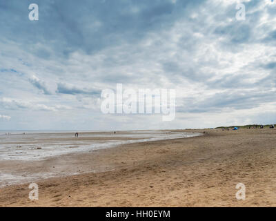Dunkle Wolken bedrohlich über einen weiten, fast menschenleer, Skegness Strand bei Ebbe. In der Ferne sehen Menschen zu Fuß am Strand. Stockfoto