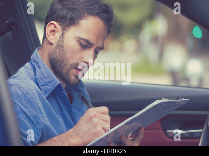 Transport und Besitz Konzept. Schönen jungen Mann im neuen Auto Lesung Signieren von Dokumenten Stockfoto