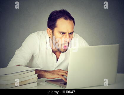 schockiert Geschäftsmann vor Laptop-Computer, die auf Bildschirm sitzen isoliert grau hinterlegt. Lustiges Gesichtsausdruck Stockfoto