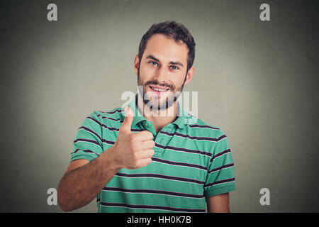 Glücklicher Mann geben Daumen nach oben Zeichen auf graue Wand Hintergrund isoliert. Positives menschliches Gesicht Ausdruck Körpersprache Stockfoto