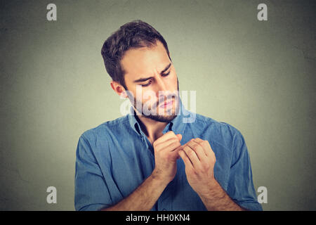 Mann, Blick auf Hände Nägel besessen über Sauberkeit Keime isoliert auf grauem Hintergrund. Emotion Gesichtsausdruck Wahrnehmung Stockfoto